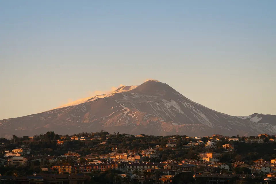 Snötäckt Etna i kvällsljus ovanför bebyggelsen i Catania