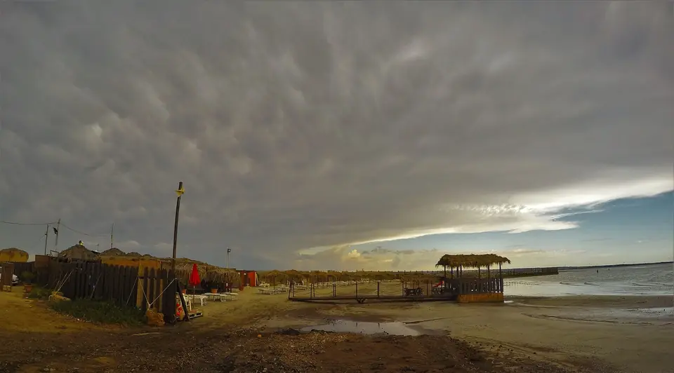 Sandstrand, parasoller och strandbyggnader vid San Teodoro i Marsala under molnig himmel