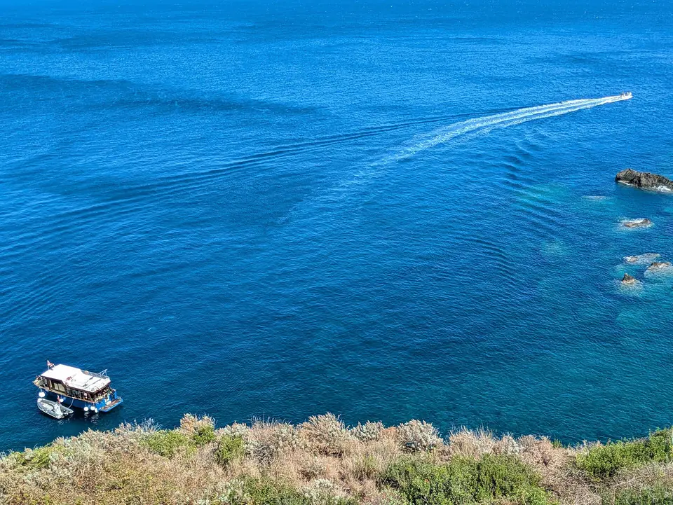 Båt vid klippkusten och en mindre båt på blått vatten vid Ustica, som illustration till dykning