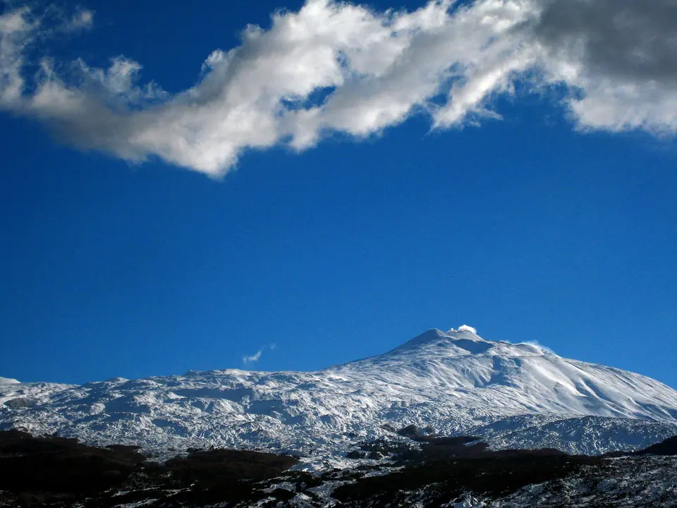 Snö på Etna mot en blå himmel med moln.