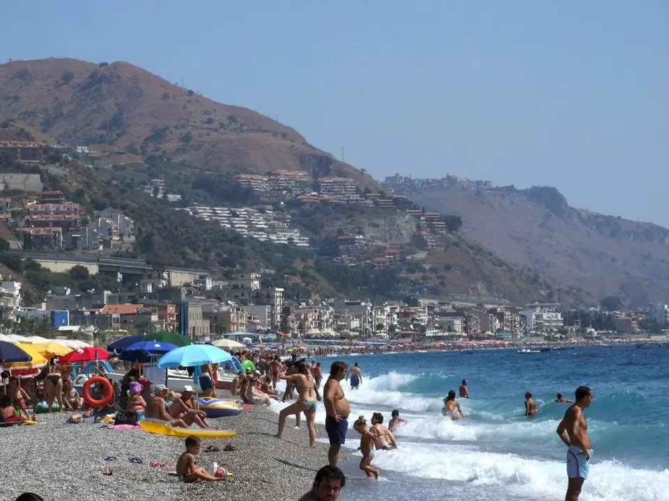 Badgäster och parasoller vid en strand nedanför Taormina.