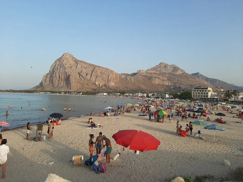 Parasoller och badgäster på San Vito Lo Capos strand med Monte Monaco i bakgrunden.
