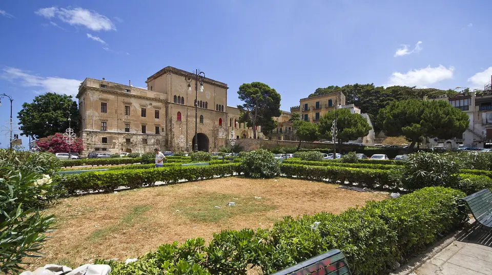 Grön trädgård framför äldre palatsbyggnader i Kalsa i Palermo