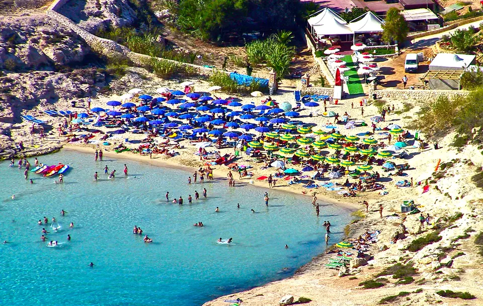 Badande och parasoller runt Cala Croces turkosa vik